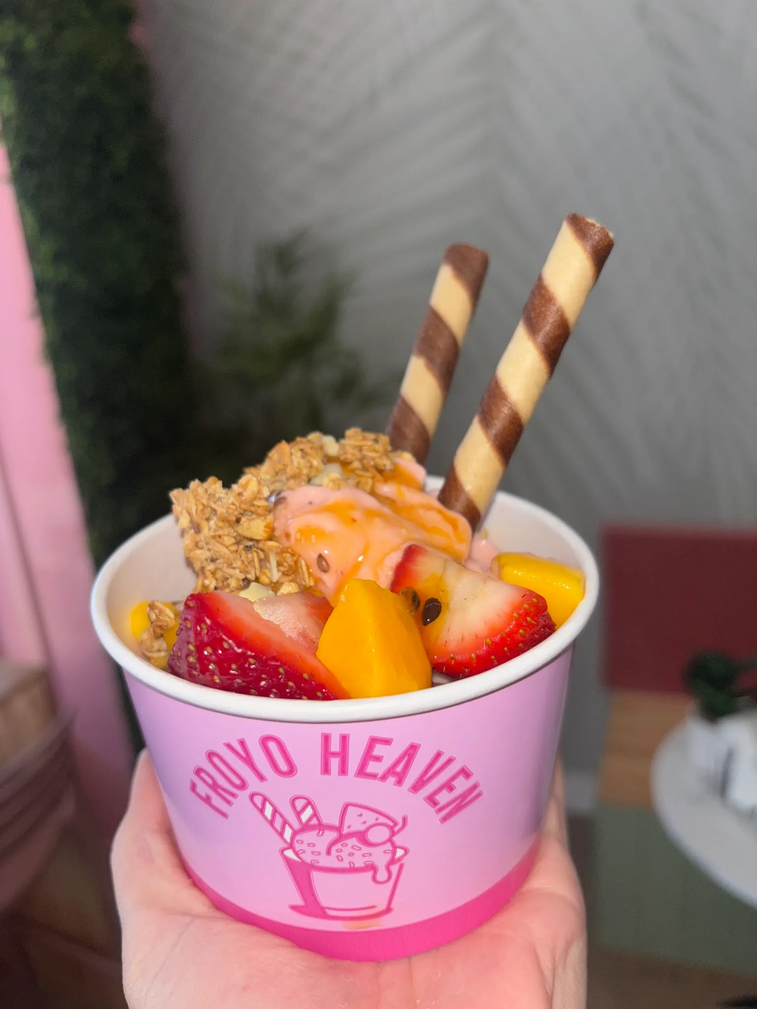 Hand holding Froyo Heaven cup with peach froyo, strawberries, mango and wafer sticks