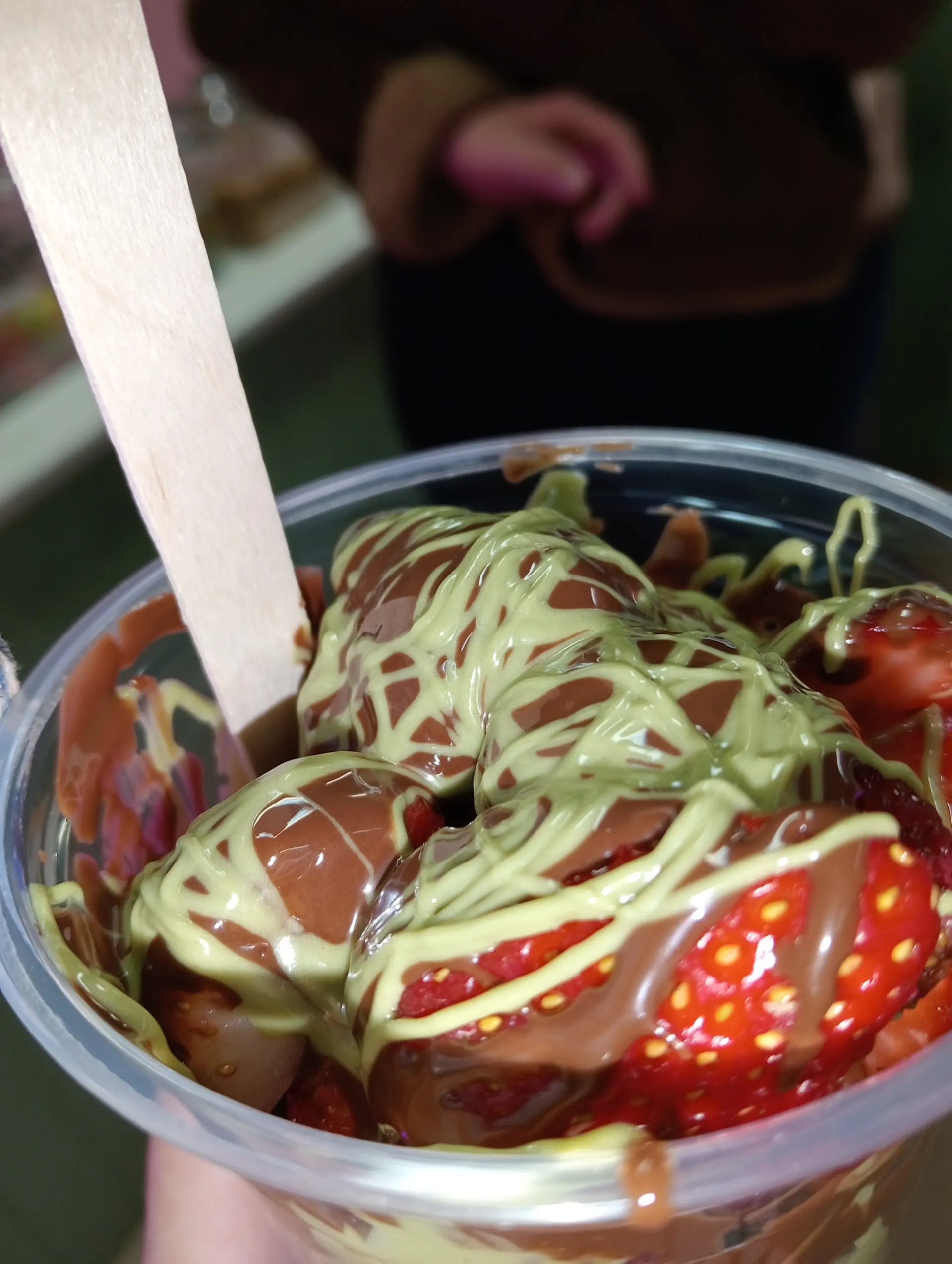 Close-up of froyo cup with matcha sauce, chocolate balls and fresh strawberries