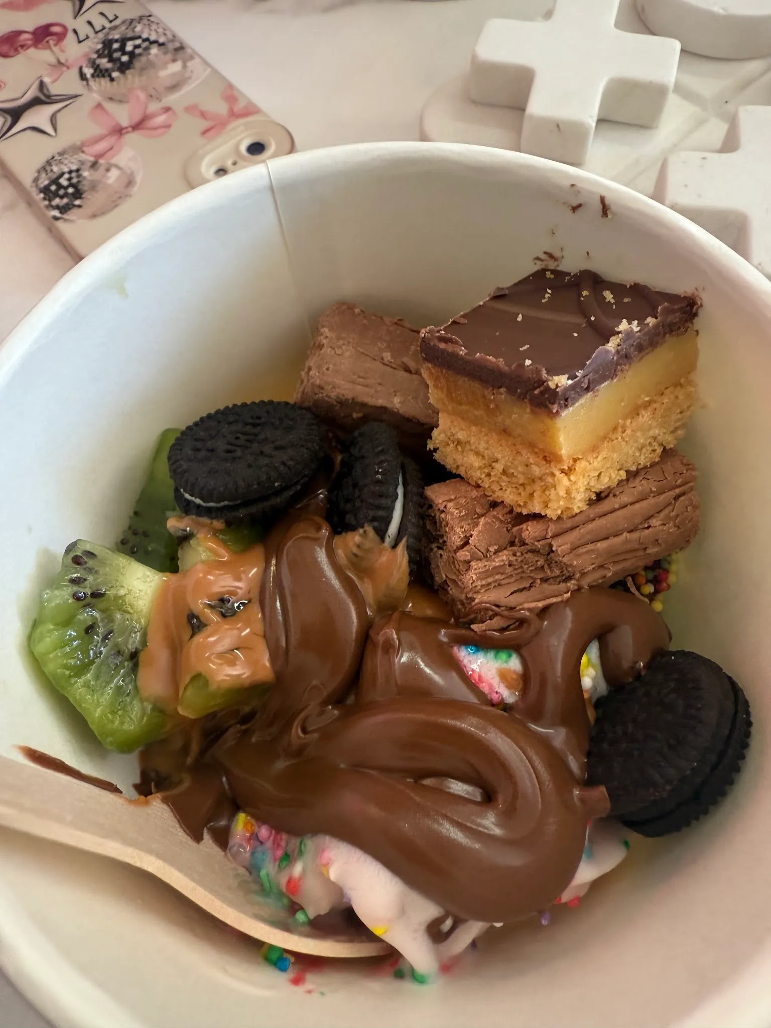 White bowl loaded with caramel slice, Oreos, kiwi and chocolate sauce