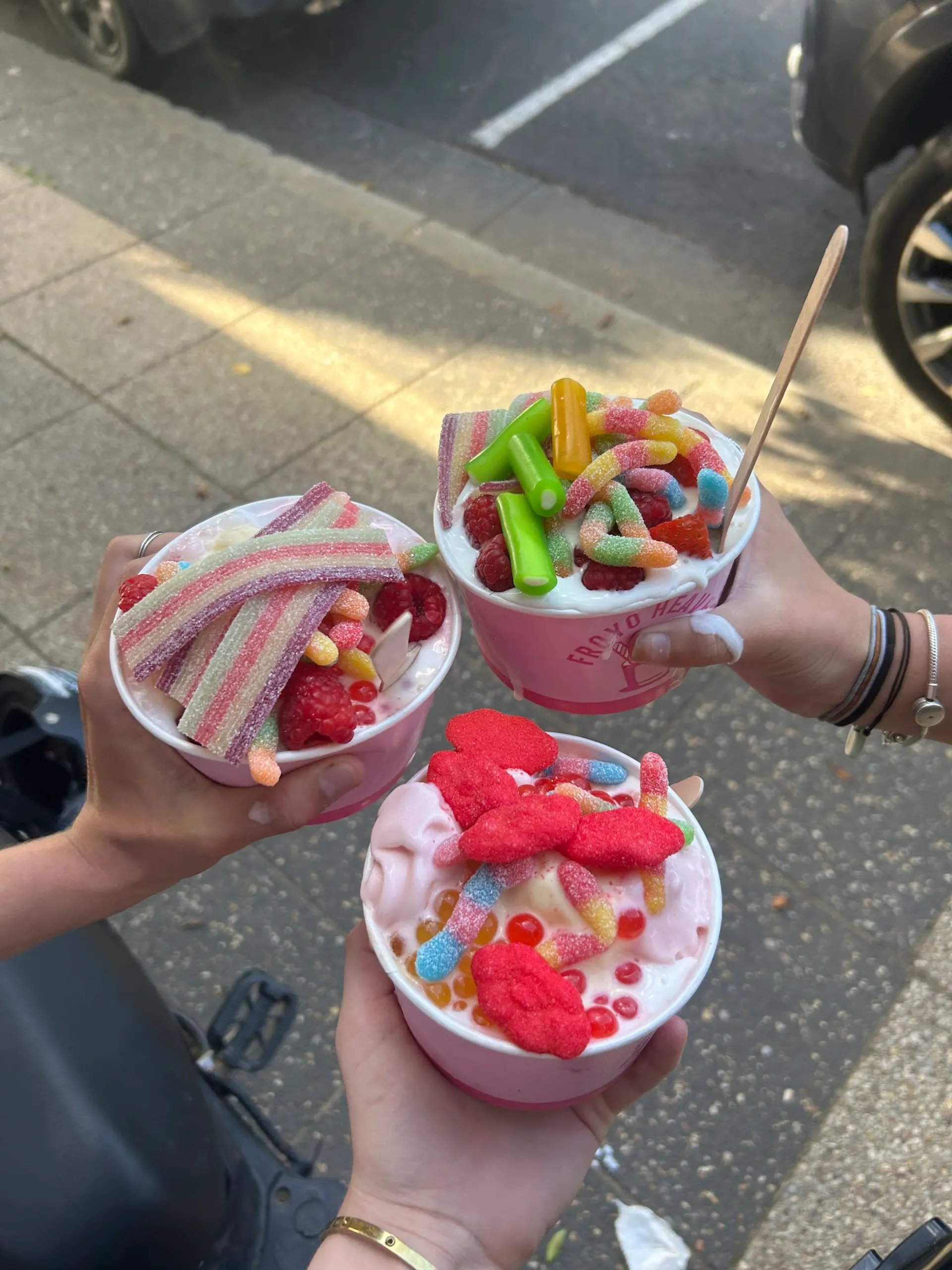 Three Froyo Heaven cups loaded with sour worms, raspberries and lolly toppings held outdoors