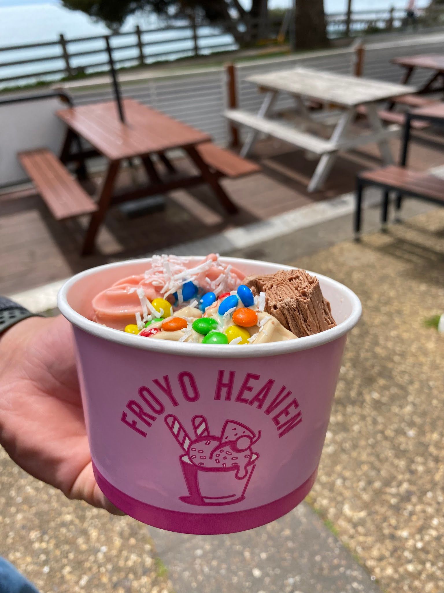 Froyo Heaven cup with M&Ms and chocolate flake held at outdoor Cowes esplanade seating
